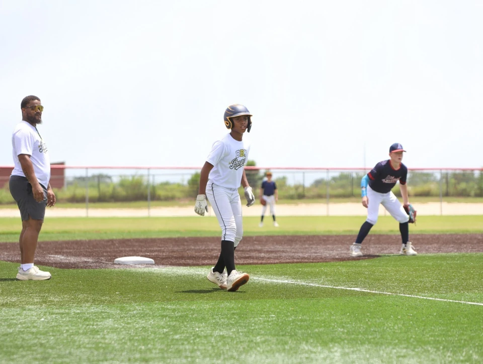 Helmeted BBN Prospects player on the basepath with a coach beside the base and a nearby fielder