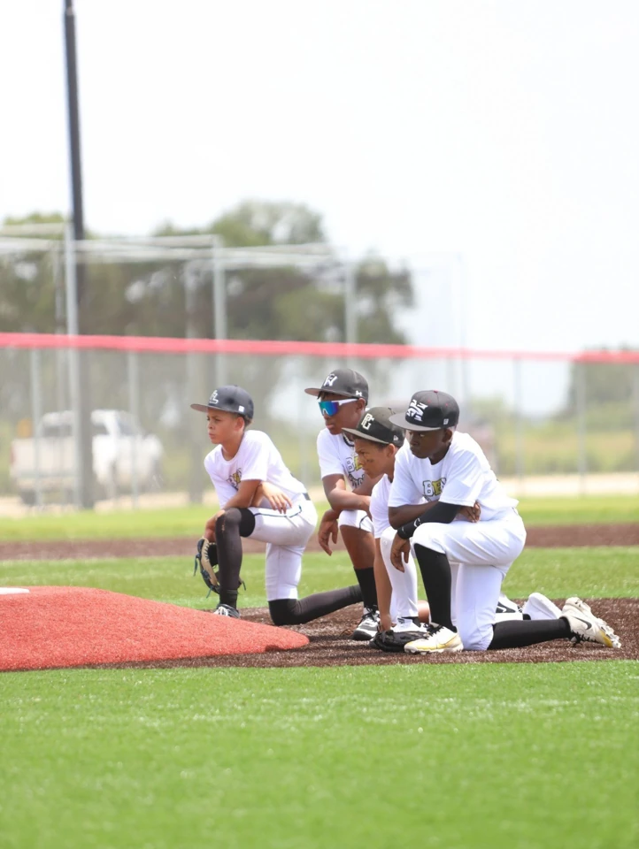 Four BBN Prospects players kneeling together beside the pitcher's mound